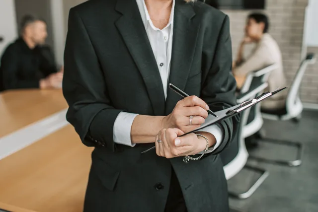 Professional in black suit taking notes during a business meeting. A sales enablement market entry checklist for teams selling into England