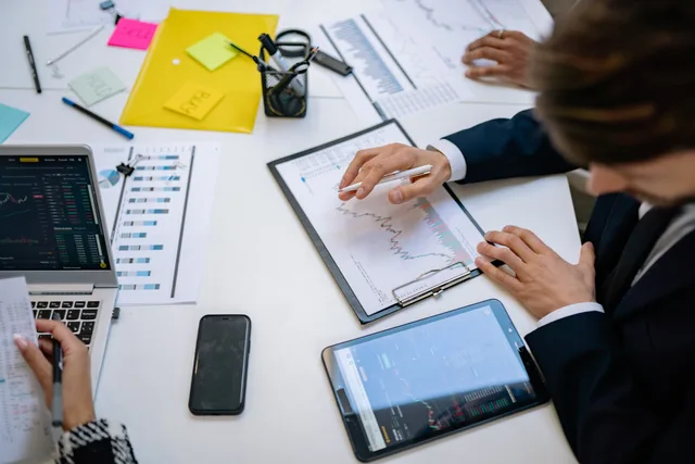 Team reviewing financial charts and digital data on tablets in an office setting. Why sales enablement measurement keeps failing your board