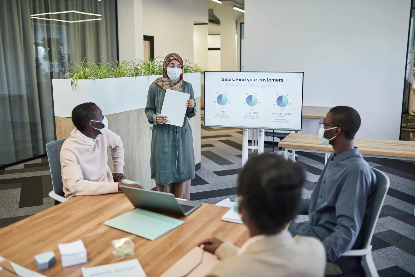 Colleagues wearing masks in a modern office discussing sales strategies.
