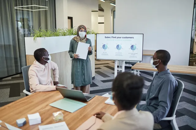 Colleagues wearing masks in a modern office discussing sales strategies. Preparing for sales enablement software selection
